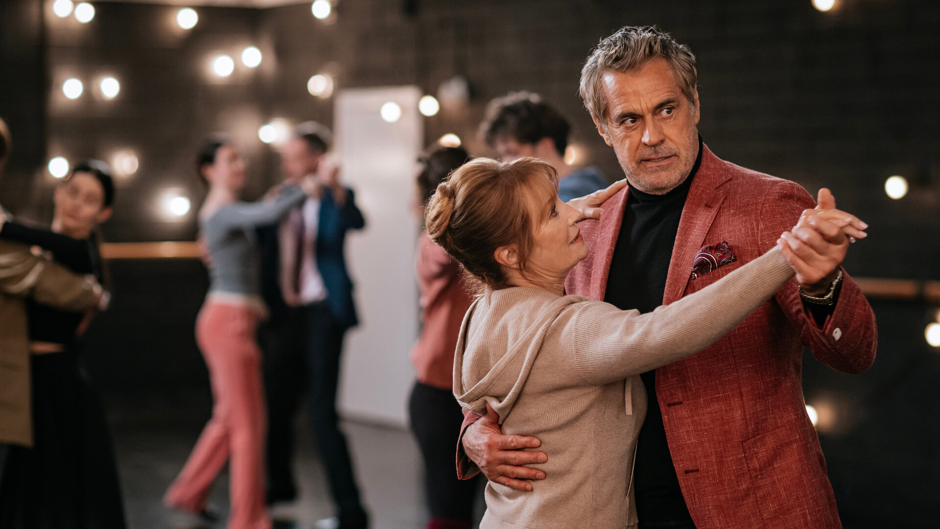 "Harry Wild - Mörderjagd in Dublin: Tanz mit dem Tod": Harry Wild (Jane Seymour) und Marcello (Edoardo Costa) tanzen in der Tanzschule miteinander. Der Raum ist dunkel, viele kleine Lampen spenden Licht. Im Hintergrund, nur verschwommen zu erkennen, tanzen drei weitere Paare.