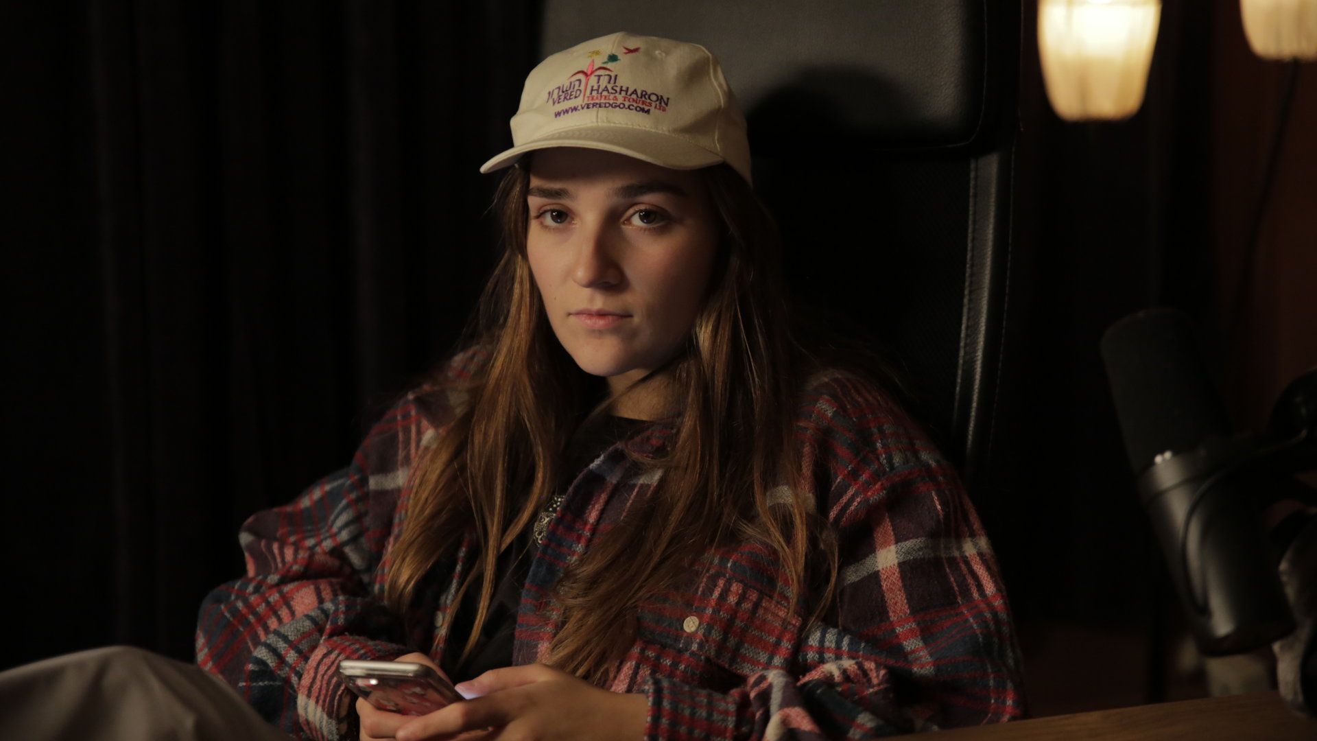 "About Saturday - Swipe der Woche": Klara (Darin Hagi) sitzt in einem dunklen Tonstudio und schaut gedankenvertieft in die Ferne, während sie ein Handy in den Händen hält.