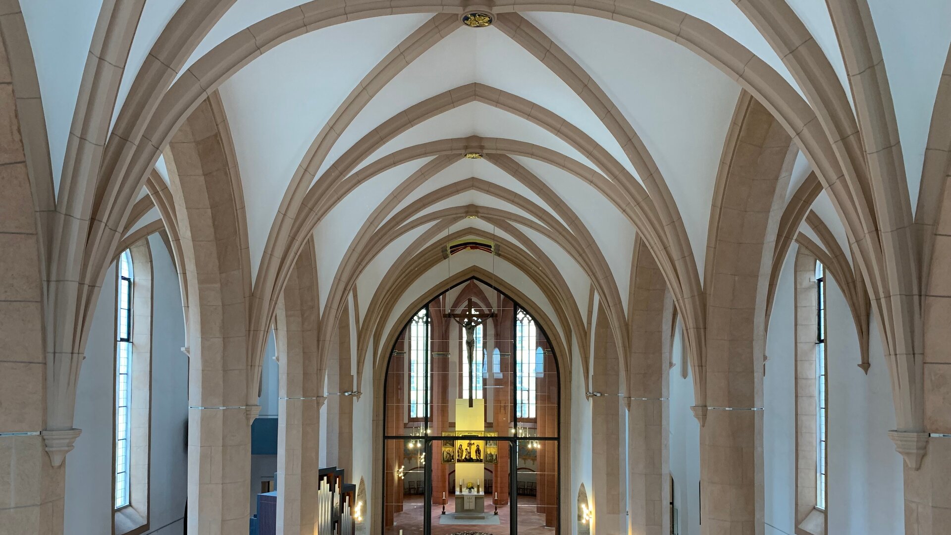 "Evangelischer Gottesdienst - Das Ungesehene sehen": Von oben sind die hellen Säulen und Bögen der St. Jakobi-Kirche in Chemnitz fotografiert. In der hinteren Bildmitte befindet  sich der Altarraum, der in ein warmes Licht getaucht ist. Über ihm hängt ein filigranes Kreuz von der Decke.