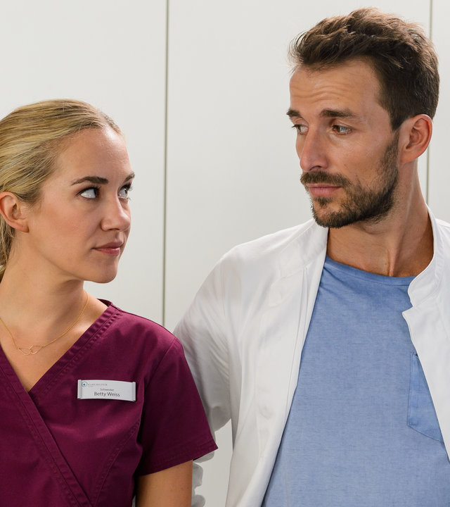 "Bettys Diagnose - Zweite Chance": Betty Weiss (Annina Hellenthal) schaut Dr. Frank Stern (Max Alberti), der neben ihr in einem Zimmer steht, sehr skeptisch an.