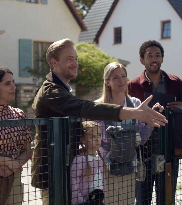 "Doppelhaushälfte - Chancengleichheit": Vor einem Gartenzaun auf dem Bürgersteig stehen die Familien Sawadi-Kröger (Helena Yousefi, Maryam Zaree, Benito Bause) und Reimers (Frederic Heidorn, Nele Kieper, Alma Löhr). Herr Reimers streckt übertrieben freundlich lächelnd seine Hand dem auf seinem Grundstück stehenden Andi Knuppe (Milan Peschel) entgegen, der den Gruß jedoch nicht erwidert.