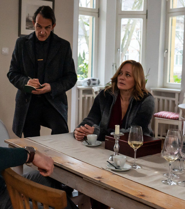"Letzte Spur Berlin - Fehlgutachten": Mina (Jasmin Tabatabai) sitzt mit Ralf Beiersdorfer (Matthias Matschke) und Sofia Kampe (Sonsee Neu) im Wohnzimmer an einem Esstisch. Radek (Hans-Werner Meyer) steht rechts von Ralf Beiersdorfer (Matthias Matschke), der verunsichert auf den Tisch schaut. Radek (Hans-Werner Meyer) schaut aufmerksam zu ihm und notiert sich seine Aussage. Der Esstisch ist belagert mit verschmutzen Weingläsern.