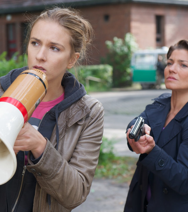 "SOKO Wismar - Genug": Martina Neuhaus (Rebecca von Mitzlaff) steht mit einem Megaphon auf einem freien Platz. Neben ihr steht Katrin Börensen (Claudia Schmutzler) mit einer Schusswaffe.