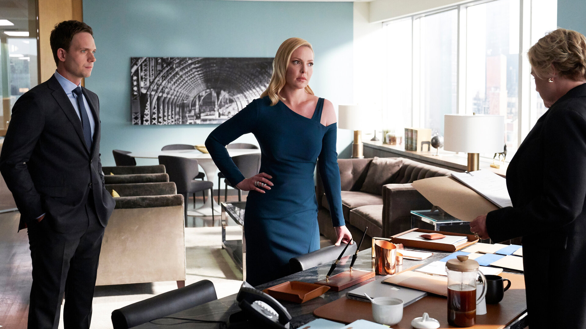 "Suits - Zur Brust hemen": Mike (Patrick J. Adams) und Samantha (Katherine Heigl)  stehen nebeneinander vor dem Schreibtisch und schauen Faye (Denise Crosby)  erwartungsvoll an, die hinter dem Schreibtisch steht und Dokumente in ihren Händen hält.