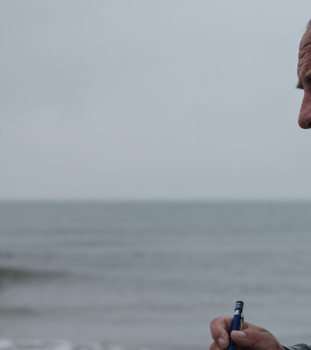 Sløborn: Polizist Mikkel Schwarting (Urs Rechn) steht mit Notizblock und Stift am Strand. Im Hintergrund sieht man die gestrandete Jacht.