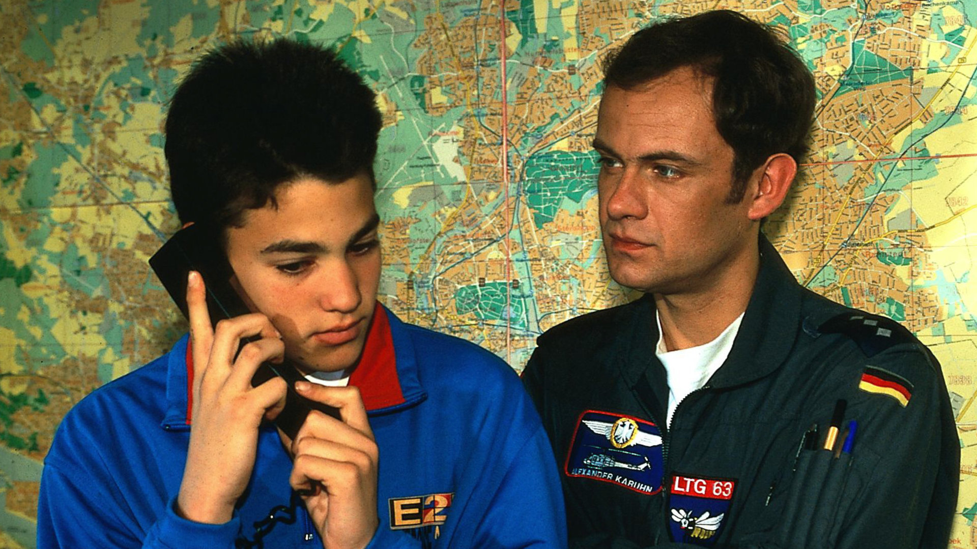 "Die Rettungsflieger - Blindflug": Benny (Pierre Britz) telefoniert, neben ihm steht Alex (Matthias Leja), an der Wand eine Landkarte.