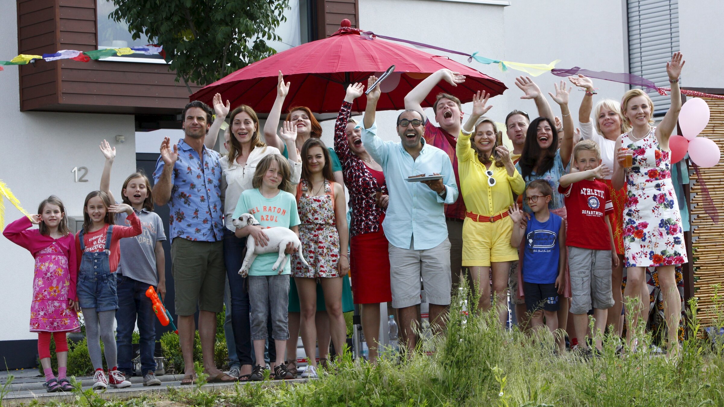 "Ein Reihenhaus steht selten allein": Mehrere Personen stehen vor einem Haus und winken in Richtung Kamera.