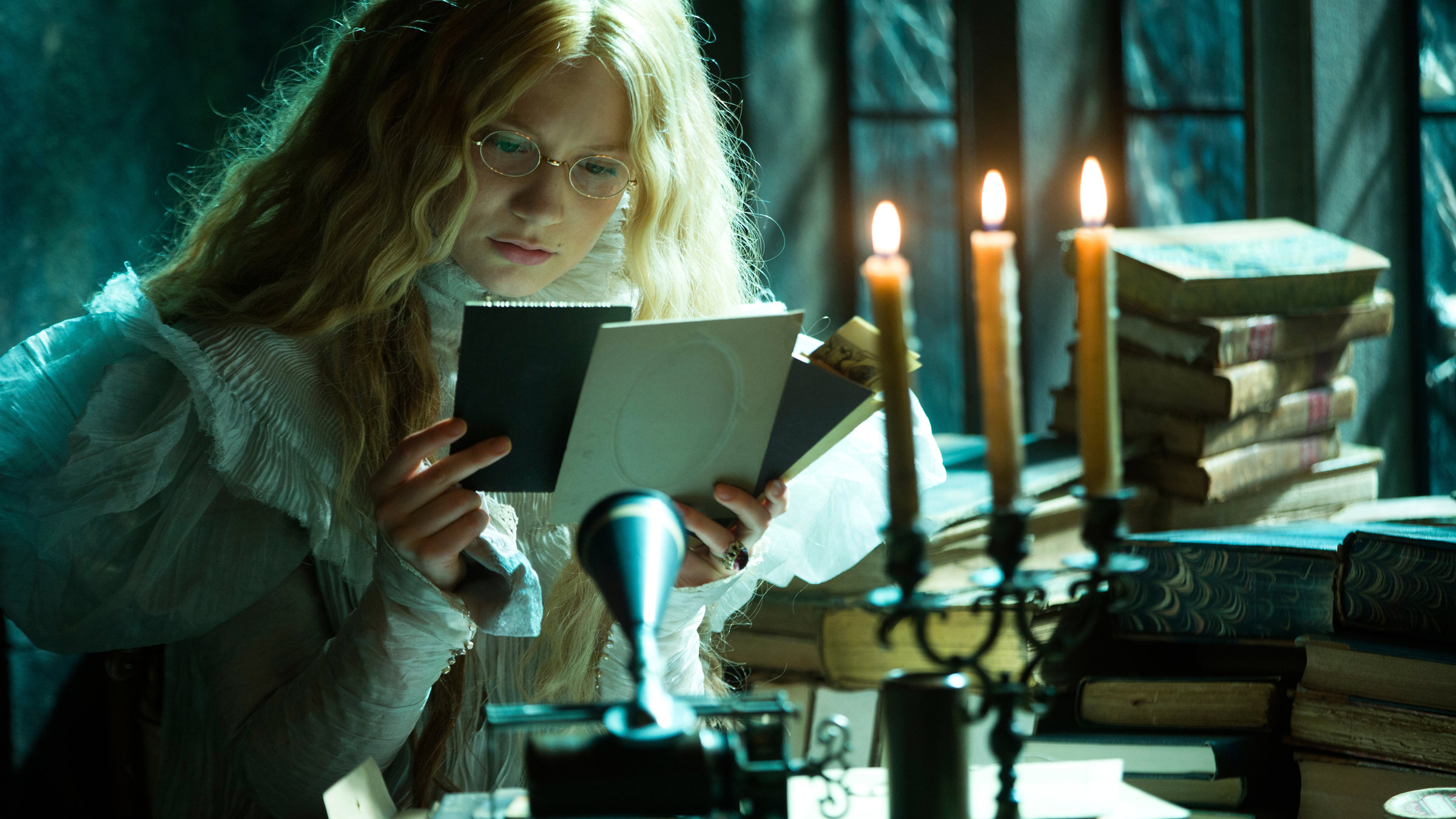 "Crimson Peak": Edith (Mia Wasikowska) sitzt bei Kerzenschein am Tisch und hält Wachsplatten in der Hand, die sie sich sehr genau anschaut.