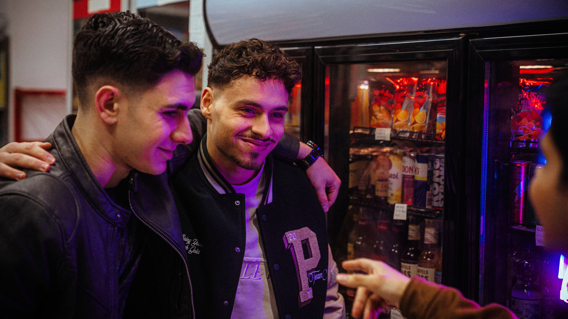 "Uncivilized - Hanau": Im Kiosk: Yasin (Mert Dincer) und Dominik (Angelo Alabiso) haben sich gegenseitig ihre Arme um die Schultern gelegt und sehen Berkan (Dennis Kharazmi) grinsend an.