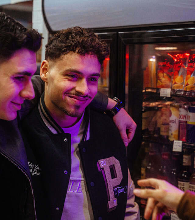 "Uncivilized - Hanau": Im Kiosk: Yasin (Mert Dincer) und Dominik (Angelo Alabiso) haben sich gegenseitig ihre Arme um die Schultern gelegt und sehen Berkan (Dennis Kharazmi) grinsend an.
