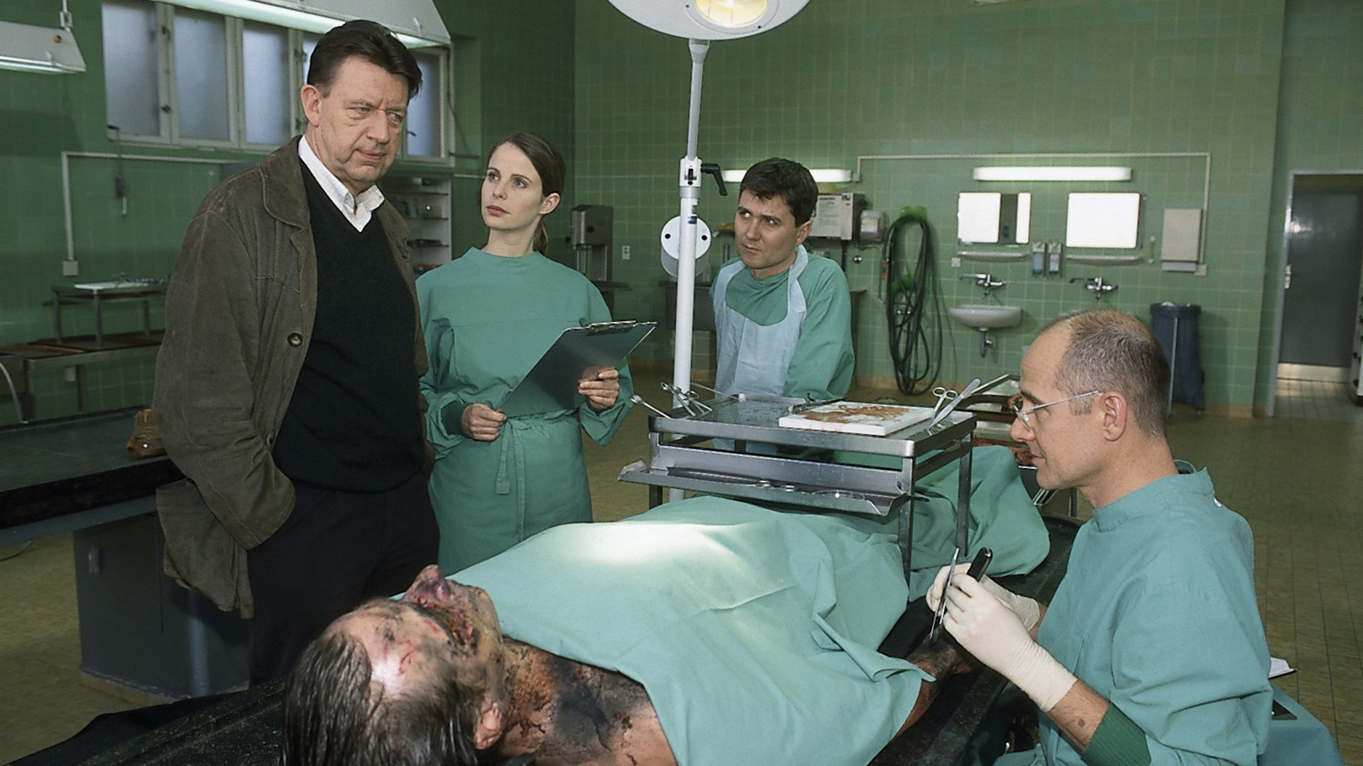 "Der letzte Zeuge - Der Fluch des letzten Königs": Gerichtsmediziner Dr. Robert Kolmaar (Ulrich Mühe), Dr. Leilah Berg (Julia Jäger) und Fred Schröder (Volker Ranisch) berichten Joe Hoffer (Jörg Gudzuhn) über ihre ersten Untersuchungsergebnisse. Sie befinden sich im Obduktionssaal.