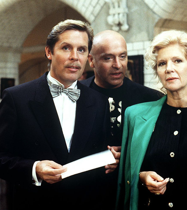 "Das Erbe der Guldenburgs - Die große Versuchung": Christine (Christiane Hörbiger), Achim (Wilfreid Baasner) und Jan Balbeck (Sigmar Solbach) stehen in einem Festsaal und unterhalten sich. Christine fächert sich mit einem Programmheft Luft zu.
