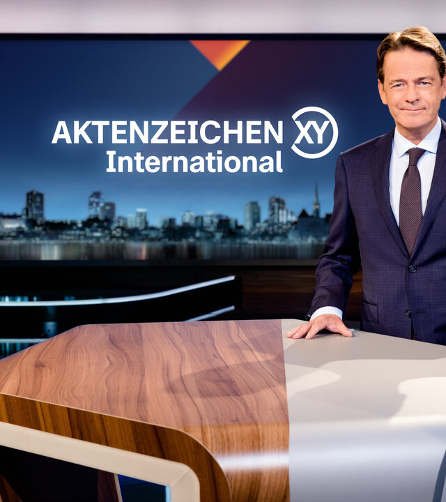 "Aktenzeichen XY... International": Rudi Cerne steht im Studio und lächelt in die Kamera.