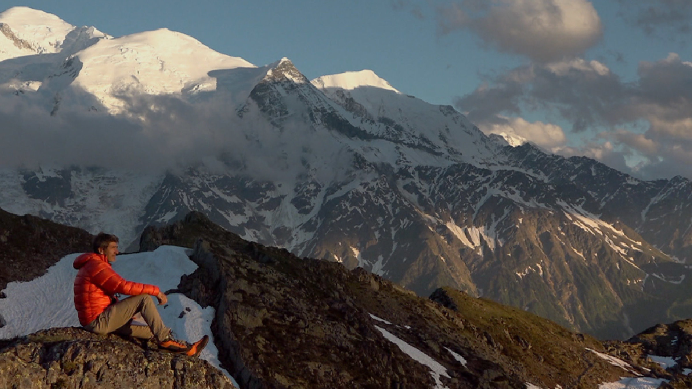 "Die große Alpenüberquerung" - ein Mensch sitzt auf einem Felsen, dahinter Bergpanorama.