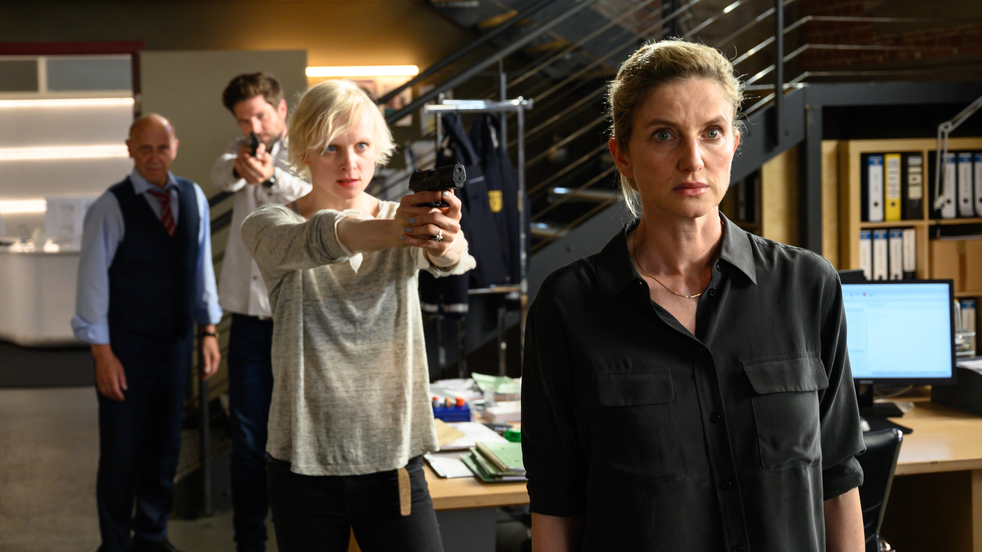 „SOKO Stuttgart - Der Pechvogel“: Luisa Kämmerlein (Anne Müller) bedroht Katja Weidemann (Elisabeth vom Koch) im Großraubüro des Präsidiums mit einer Waffe. Michael Kaiser (Karl Kranzkowski) und Jo Stoll (Peter Ketnath) kommen ihrer Kollegin zu Hilfe: Jo Stoll zielt mit seiner Waffe auf Luisa Kämmerlein, während Michael Kaiser auf sie einredet.