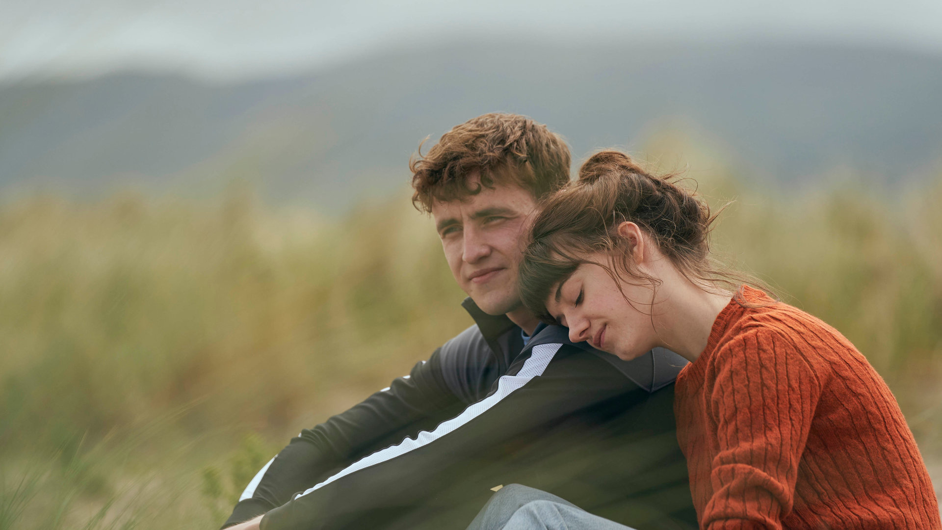 "Normal People - Heilung": Marianne (Daisy Edgar-Jones) und Connell (Paul Mescal) sitzen gemeinsam an einem Strand. Während Connell ernst zur Seite schaut, legt Marianne ihren Kopf auf seine Schulter.