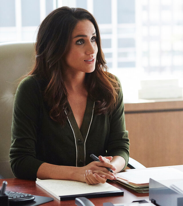 "Suits - Entgleist": Rachel (Meghan Markle) sitzt im Büro an einem Schreibtisch. Ihre Hände sind ineinandergelegt, halten einen Stift und liegen auf der Tischplatte auf einem Block.