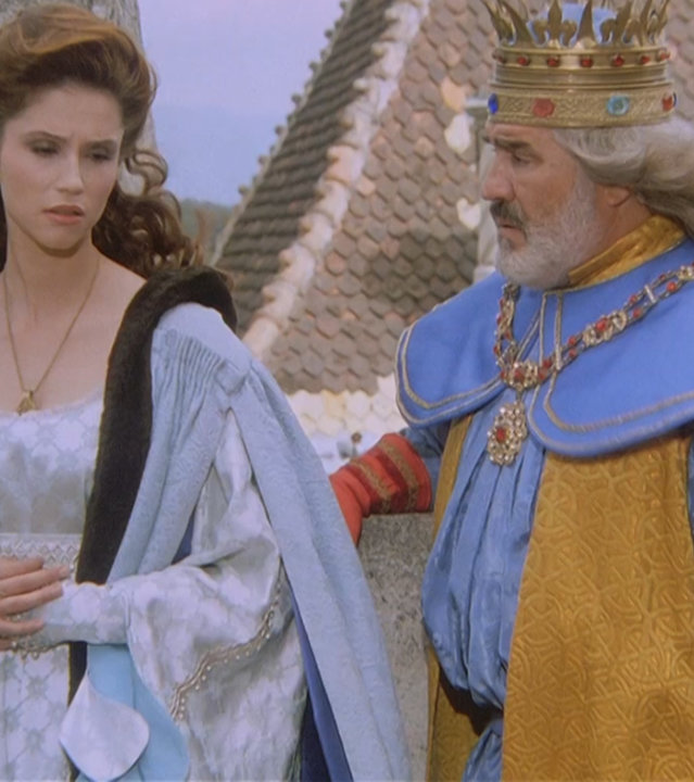 "Prinzessin Fantaghirò - Teil 4": Prinzessin Fantaghirò (Alessandra Martines) und ihr Vater (Mario Adorf) stehen auf einer Zinne der königlichen Burg. Sie steht links und blickt traurig zu Boden. Ihr Vater steht rechts von ihr und schaut sie besorgt an.