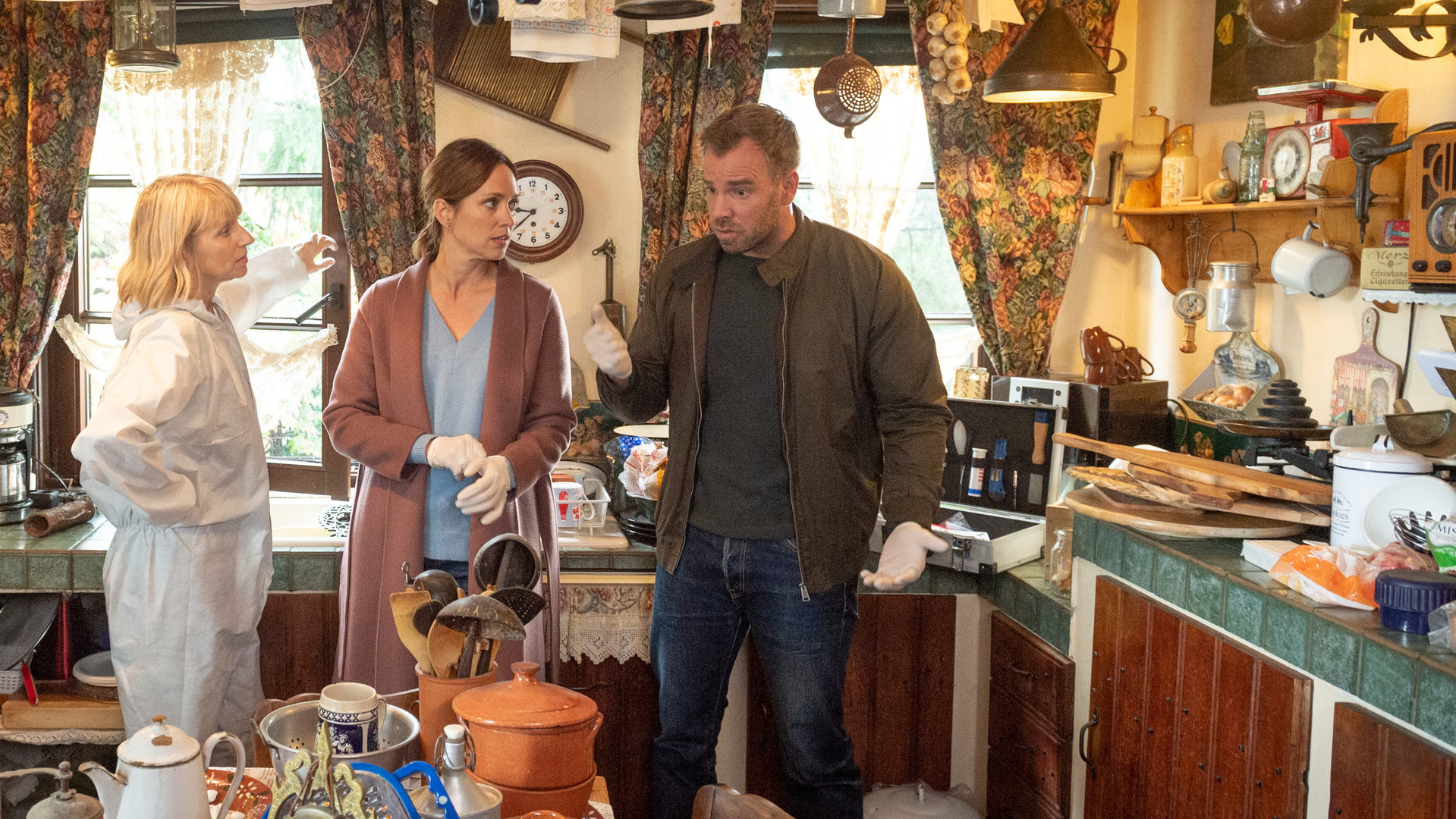 "SOKO Wismar – Kunst und Krempel": Roswitha Prinzler (Silke Matthias), Karoline Joost (Nike Fuhrmann) und Lars Pöhlmann (Dominic Boeer) stehen in einer Küche und besprechen sich. Überall stapelt sich Geschirr, Keramik, und Gebrauchsgegenstände stehen herum.