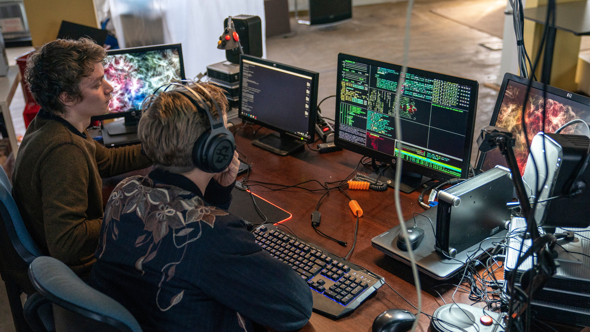 "The Bank Hacker": Andy (Joren Seldeslachts) und Jeremy (Tijmen Govaerts) sitzen gemeinsam vor mehreren Bildschirmen und blicken in diese hinein. Andy trägt Kopfhörer.