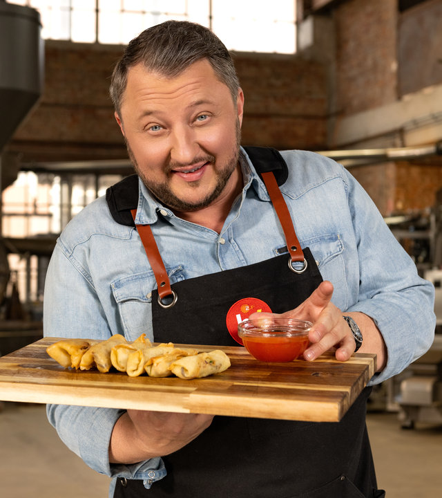"ZDFbesseresser: Die Tricks der Asia-Restaurants - Sebastian Lege deckt auf": Produktentwickler Sebastian Lege trägt ein Holztablett. Darauf liegen sechs Frühlingsrollen. In seiner linken Hand hält er eine Glasschale mit süßsaurer Sauce.