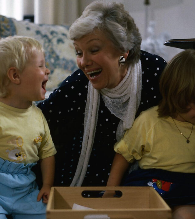 "Die Wicherts von nebenan: Die Heide, Hannelore und Hotels": Hannelore (Maria Sebaldt) sitzt im Wohnzimmer vor der Couch zwischen ihren Enkelkindern Sebastian (Oliver Lausberg) und Klein-Katrinchen (Sophie Birkner) und hat ganz viel Spaß.