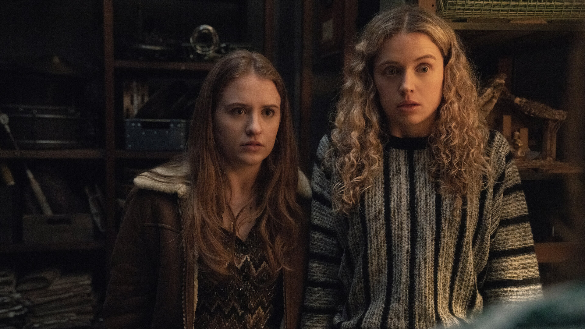 "Extraordinary - Die Jen-Show": Jen (Máiréad Tyers) und Carrie (Sofia Oxenham) stehen in einem Raum mit hohen Regalen und blicken schockiert geradeaus.