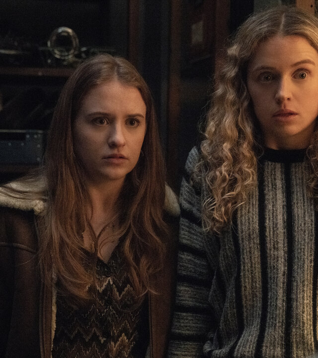 "Extraordinary - Die Jen-Show": Jen (Máiréad Tyers) und Carrie (Sofia Oxenham) stehen in einem Raum mit hohen Regalen und blicken schockiert geradeaus.