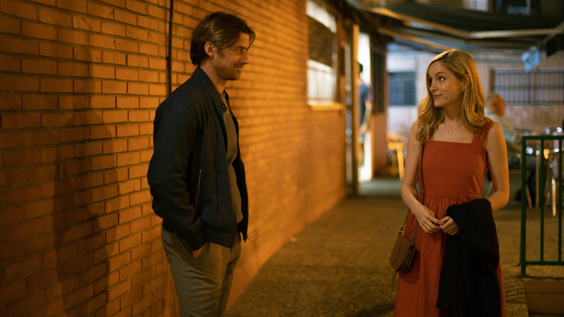 "The Diplomat - Die Verhaftung": Laura Simmonds (Sophie Rundle) und Fabian Hartmann (Philipp Boos) stehen im Schein einer Lampe vor einem Gebäude und lächeln sich an.