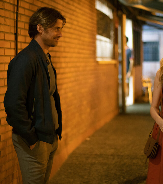 "The Diplomat - Die Verhaftung": Laura Simmonds (Sophie Rundle) und Fabian Hartmann (Philipp Boos) stehen im Schein einer Lampe vor einem Gebäude und lächeln sich an.