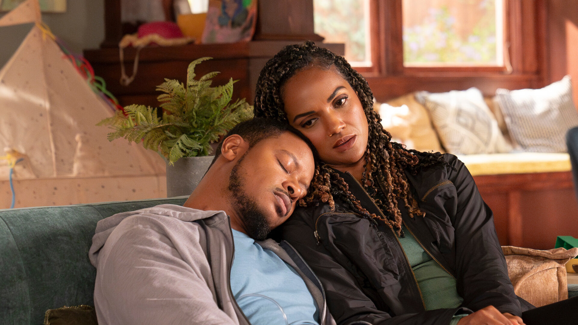 "The Rookie - Chaos": James Murray (Arjay Smith) und Detective Harper (Mekia Cox) sitzen zusammen auf einem Sofa in einem Wohnzimmer. Beide tragen Alltagskleidung. James hat seinen Kopf auf Harpers Schulter gelegt und sie schmiegt wiederum ihren Kopf an seinen an. Seine Augen sind geschlossen, während sie nach vorn blickt.