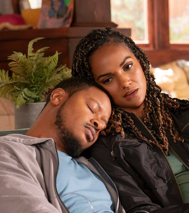 "The Rookie - Chaos": James Murray (Arjay Smith) und Detective Harper (Mekia Cox) sitzen zusammen auf einem Sofa in einem Wohnzimmer. Beide tragen Alltagskleidung. James hat seinen Kopf auf Harpers Schulter gelegt und sie schmiegt wiederum ihren Kopf an seinen an. Seine Augen sind geschlossen, während sie nach vorn blickt.