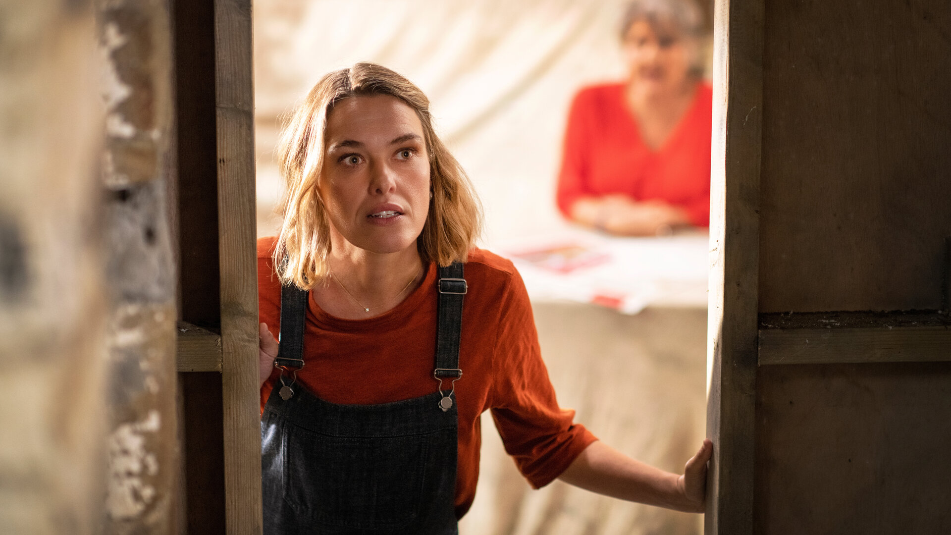 "Beyond Paradise - Verschwunden": Martha (Sally Bretton) öffnet eine Tür und schaut nach draußen. Im Hintergrund sitzt unscharf ihre Mutter Anne (Barbara Flynn) an einem Tisch.