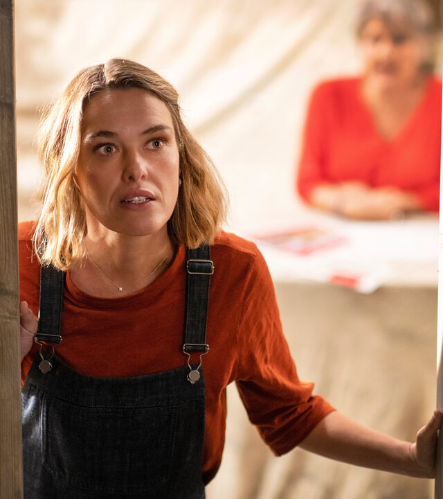 "Beyond Paradise - Verschwunden": Martha (Sally Bretton) öffnet eine Tür und schaut nach draußen. Im Hintergrund sitzt unscharf ihre Mutter Anne (Barbara Flynn) an einem Tisch.