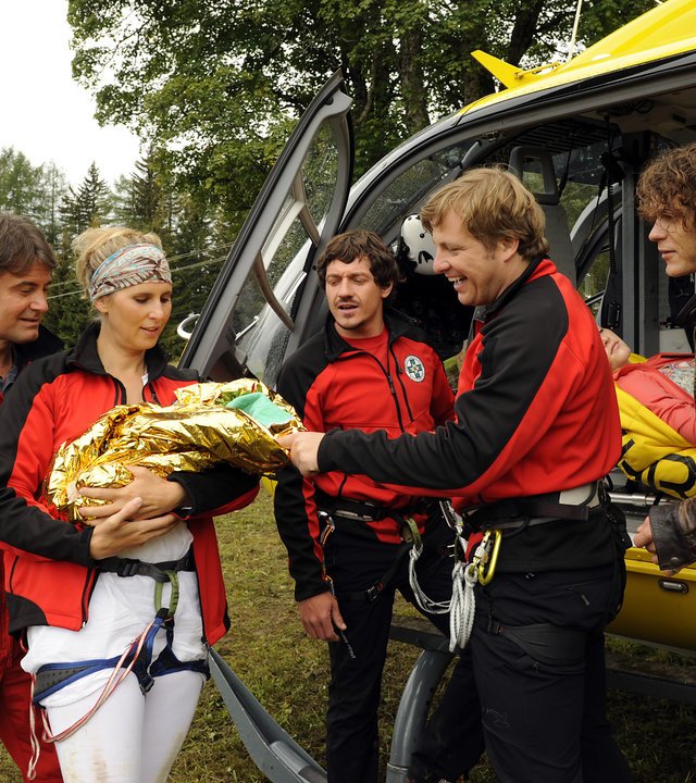 "Die Bergretter - Auf der Flucht": Die Retter Michael (Robert Lohr), Bea (Paula Paul), Tobias (Markus Brandl) und Toni (Martin Klempnow) stehen mit dem geretteten Baby vor ihrem Hubschrauber. Daneben steht Ronnie (Marlon Kittel), der Vater des Babys.