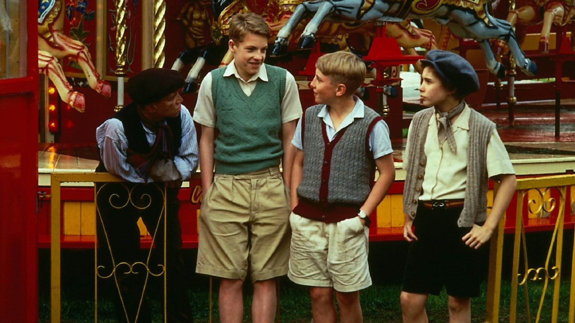 "Fünf Freunde jagen die Entführer": Spikey (Lee Barrett), Julian (Marco Williamson), Dick (Paul Child) und Jo (Vanessa Cavanagh) stehen nebeneinander vor einem Kinderkarussell und blicken sich nachdenklich an.