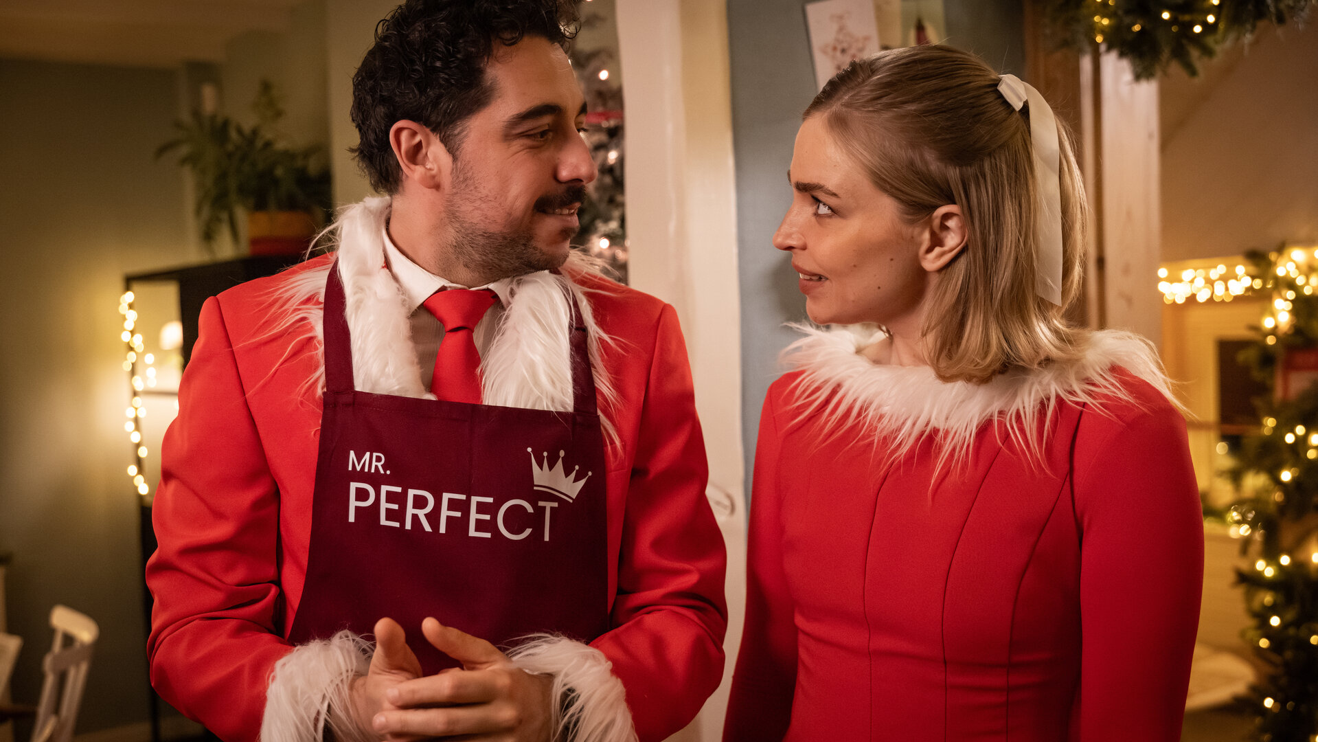 "Single Bells - Only Losers for Annie? - Damien (II)": Roel (Robbert Vervloet) und Mina (Julie Van den Steen) stehen in ihren vom Weihnachtsmann inspirierten Anzug und Kleid nebeneinander. Sie schauen sich intensiv an.