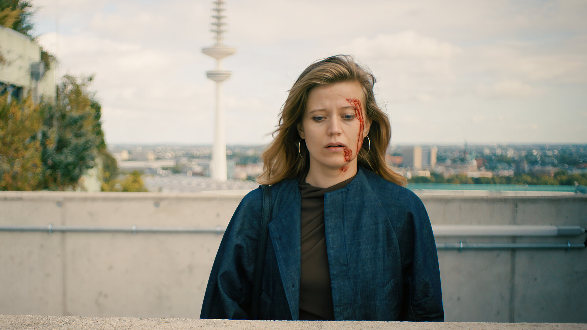 "Notruf Hafenkante - Dunkelrot": Milena Harnisch (Camille Dombrowsky) steht auf einer Dachterrasse. Sie blickt nachdenklich. Auf ihrer linken GesichtshÃ¤lfte befinden sich Blutspuren. Im Hintergrund liegt das Stadtpanorama von Berlin mit dem Funkturm.
