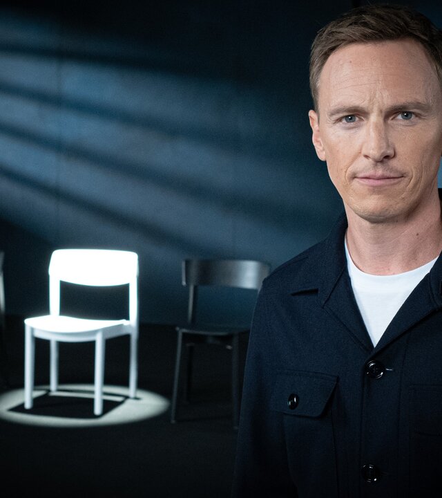 "Weil du mir gehörst! - Wenn Männer ihre Frauen töten": Jochen Breyer steht in einem abgedunkelten Raum und schaut in die Kamera. Im Hintergrund stehen mehrere Stühle, ein weißer Stuhl wird angestrahlt.