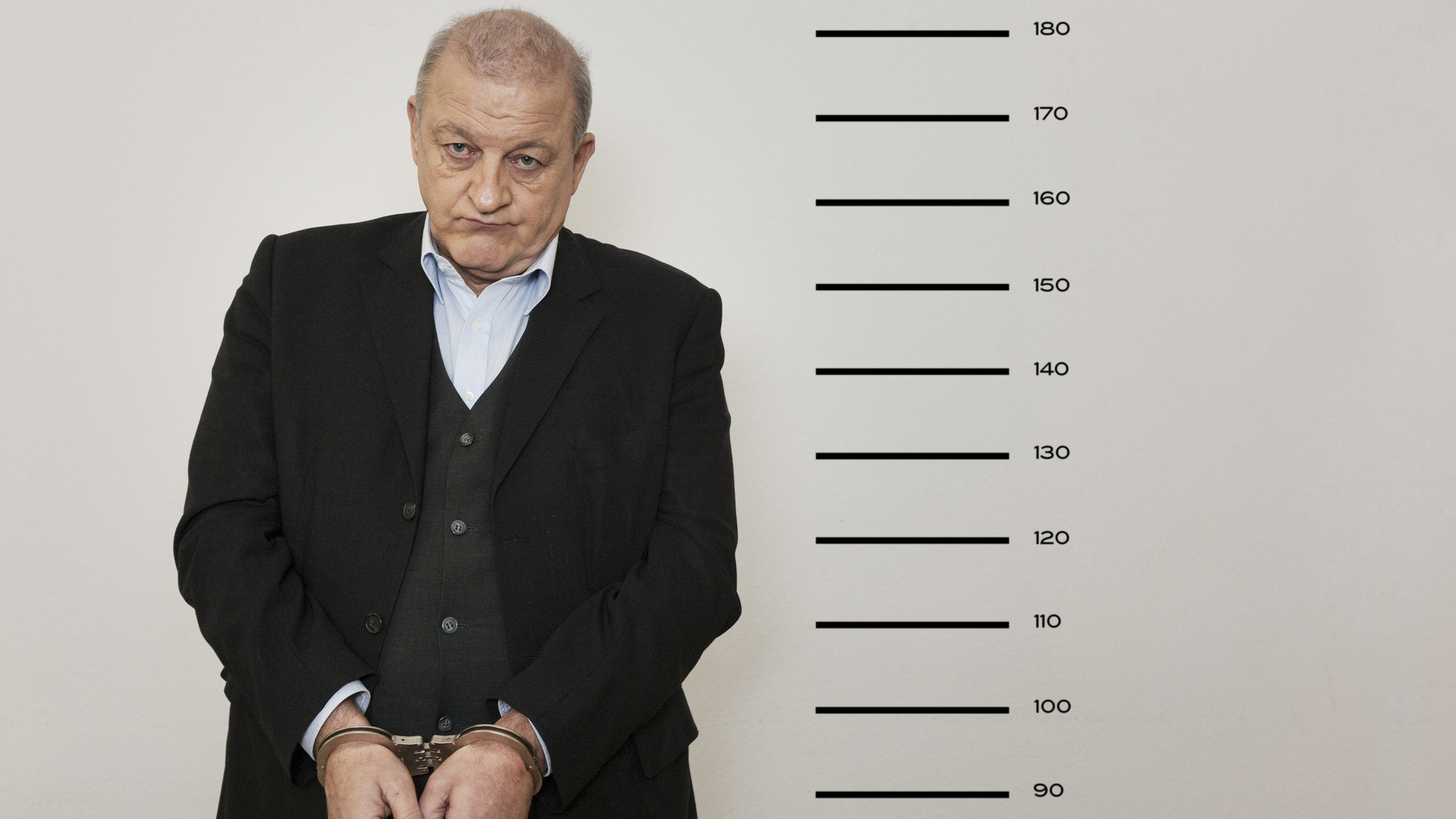 "Wilsberg – Kein Weg zurück": Ein Gefängnis-Portrait von Georg Wilsberg (Leonard Lansink), der in Handschellen neben einer Messlatte steht.