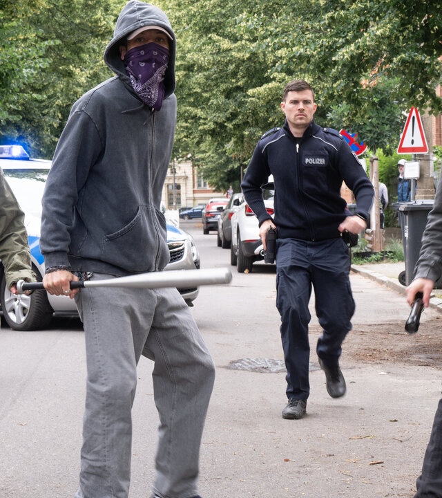 "SOKO Potsdam - Eure Welt, unsere Welt": Drei Jugendliche stehen - mit Bandana-Tüchern maskiert - konfrontierend auf der Straße. Der Jugendliche in der Mitte hält einen silbernen Baseballschläger in der Hand. Hinter den Jugendlichen kommt ein Polizist (Komparse) angelaufen.