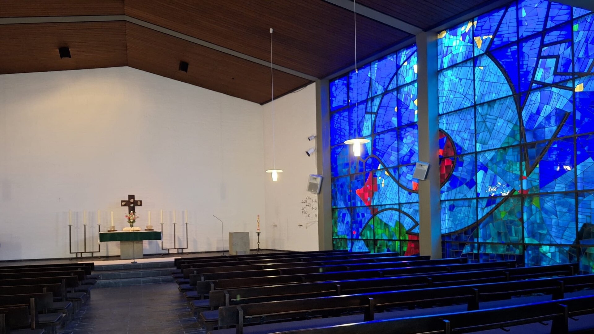 "Evangelischer Gottesdienst - Von Seifenblasen und Auferstehung": Im Inneren der Pauluskirche in Marburg steht ein schlichter Altar vor einer weißen Wand zu, davor stehen die dunklen Kirchenbänke. Dazu auffällig im Kontrast ist das große, farbintensive, hauptsächlich in kräftigem Blau gehaltenen Fenster, das vom Boden bis zur Decke reicht.