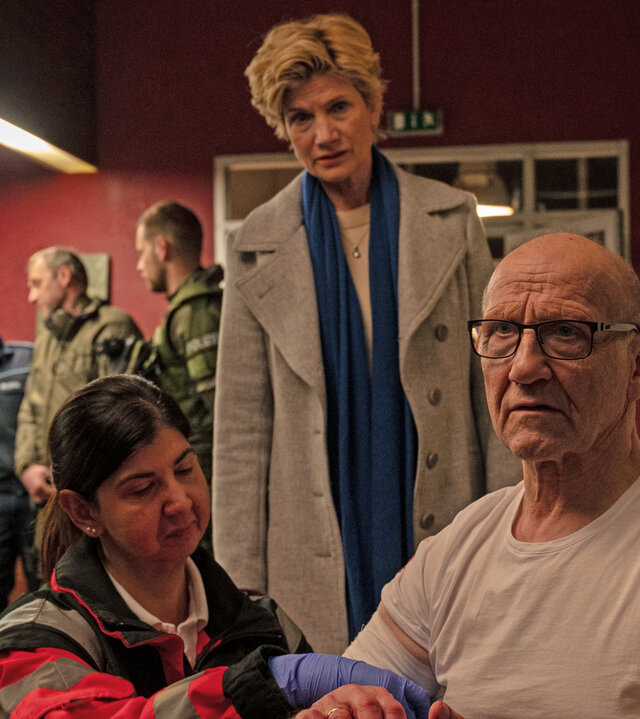 "SOKO Stuttgart - Kaiser im Visier": Kriminaldirektor Michael Kaiser (Karl Kranzkowski) bekommt neben der Wache im Präsidium von einer Notfallsanitäterin (Komparsin) einen Verband angelegt. Er schaut nachdenklich ins Leere. Hinter den beiden steht die Erste Kriminalhauptkommissarin Martina Seifert (Astrid M. Fünderich) und schaut Kaiser besorgt an. An der Wache im Hintergrund stehen Polizei- sowie SEK-Beamte und beraten sich.
