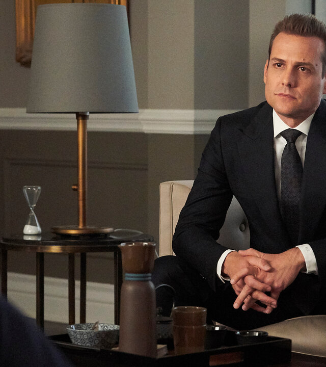 "Suits - Katzen, Ballett, Harvey Specter": Harvey (Gabriel Macht) - in einem dunklen Anzug - sitzt auf einem Sofa und schaut angespannt. Links neben ihm stehen auf einem Beistelltisch eine Lampe und eine Sanduhr.