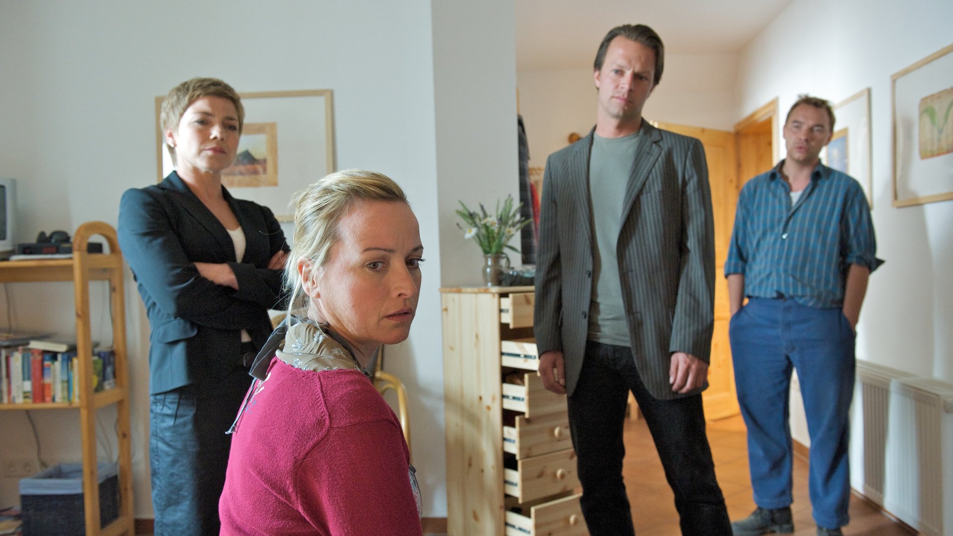 "SOKO Wismar - Frau Neumann": Irene Lüders (Katharina Abt) sitzt abgewandt von den Ermittlern im Zimmer von Frau Neumann, das von den Kommissaren Katrin Börensen (Claudia Schmutzler) und Sven Herzog (Michael Härle) durchsucht wurde. Die Schubladen einer Holzkommode stehen noch offen. Ihr Bruder Ralf Lüders (Thomas Arnold) steht im Flur und beobachtet die Szene.