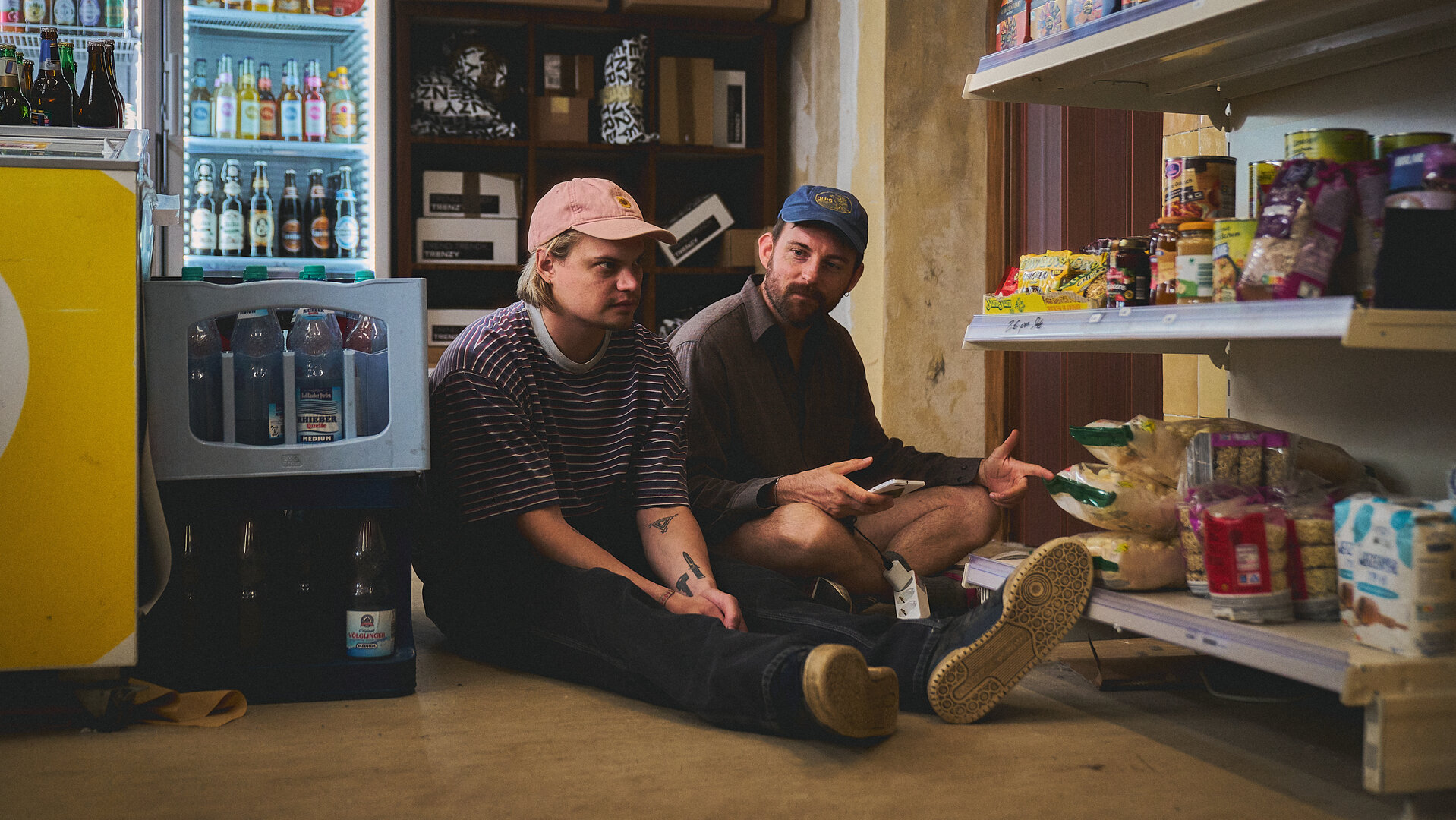 "Späti - Grumpy Elster": Fred (Wilson Gonzalez) und Konnopke (Alexander Finkenwirth) sitzen im Späti auf dem Boden und hören Musik.