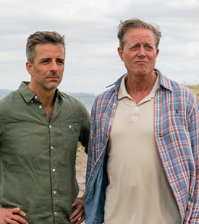 "Dan Sommerdahl - Tödliche Idylle: Liebeslabyrinth": Flemming Torp (André Babikian) und Dan Sommerdahl (Peter Mygind) stehen am Meer vor einer Düne. Es ist windig.