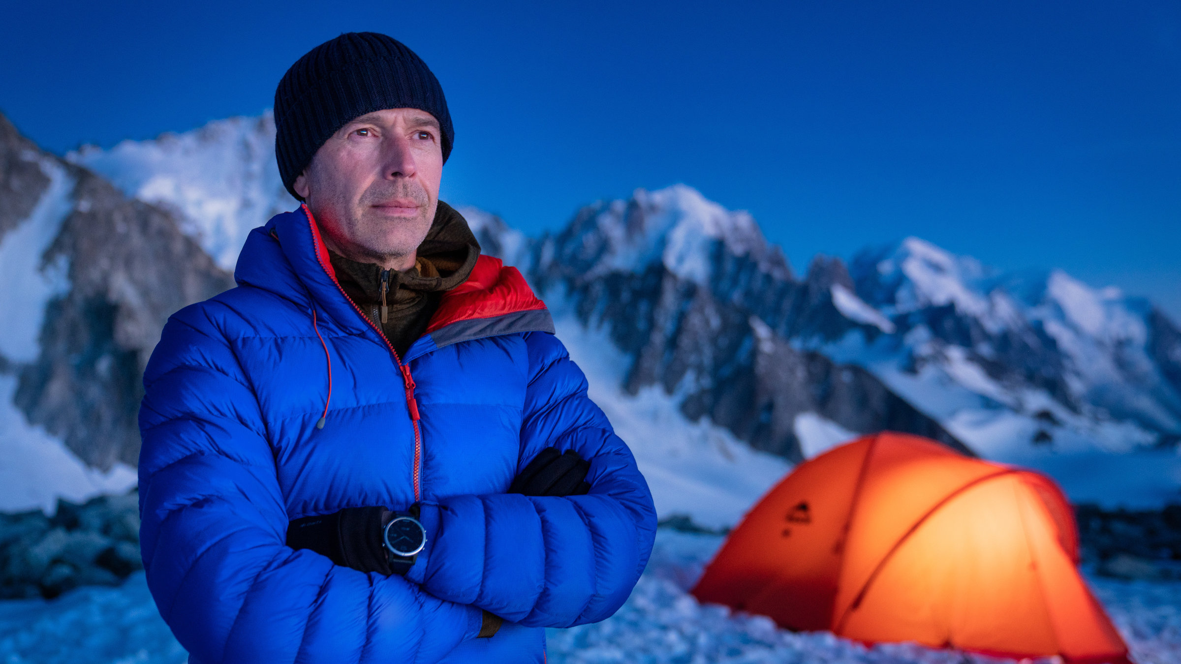 "Faszination Erde: Die Alpen - Nichts ist für die Ewigkeit": Dirk Steffens steht im Abendlicht auf dem Mont Blanc Massiv vor einem von innen heraus erleuchteten Zelt.