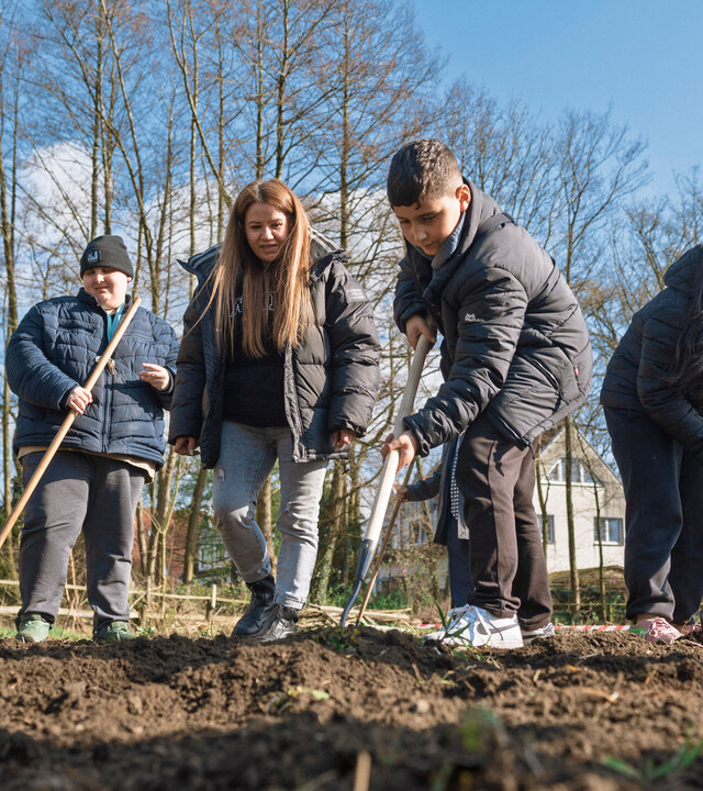 "Aktion Mensch - Glückszahlen der Woche": Fünf Personen arbeiten im Garten. Sie bearbeiten ein Stück Land mit ihren Rechen. Im Hintergrund stehen Bäume, der Himmel ist blau.