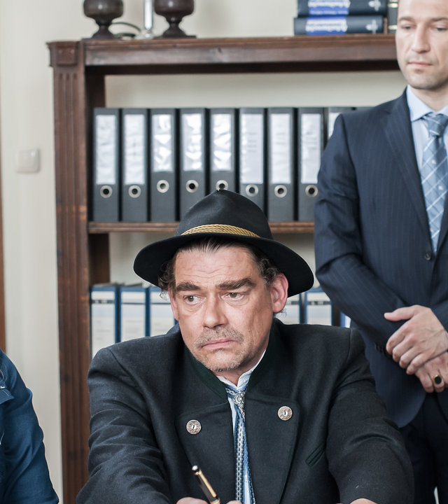 "Der Bergdoktor - Alte Wunden (2)": Anne (Ines Lutz) sitzt an einem Tisch neben Arthur (Martin Feifel), der einen Stift in der Hand hält. Hinter ihnen steht der Notar (Timo Senff).
